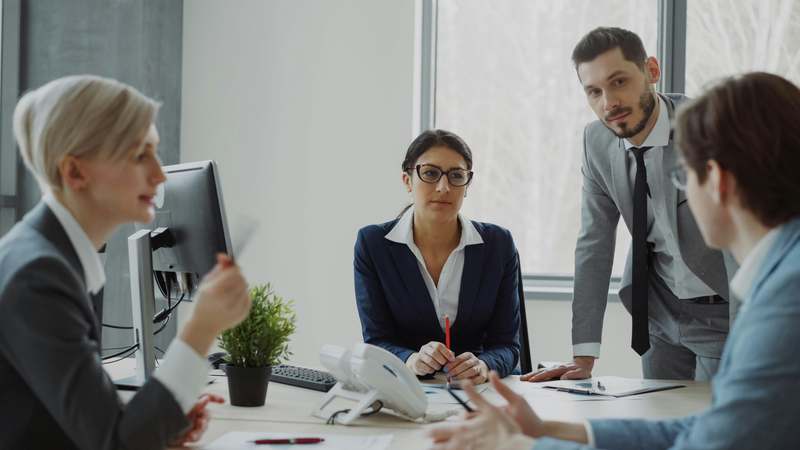 Diverse group of professionals exchanging ideas at a light-filled modern co-working space, one person holding a notebook labeled 'My Next Chapter'
